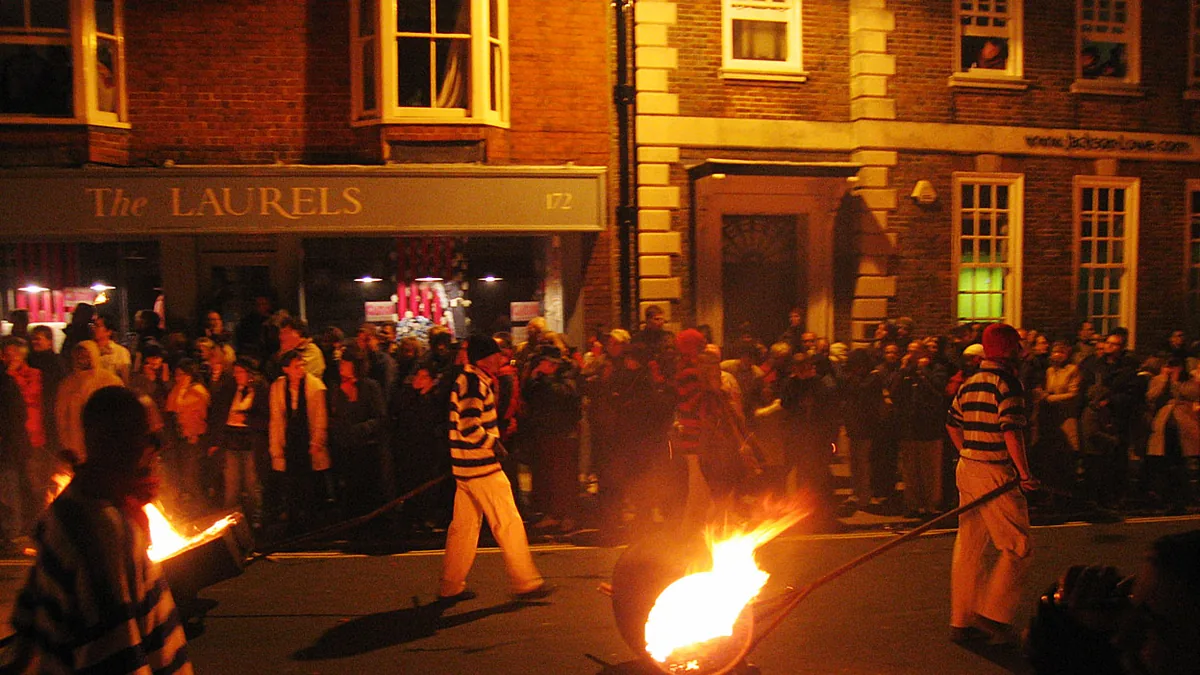 Cliffe Bonfire Society members in striped jerseys dragging burning tar barrels along a Lewes street, watched by a crowd