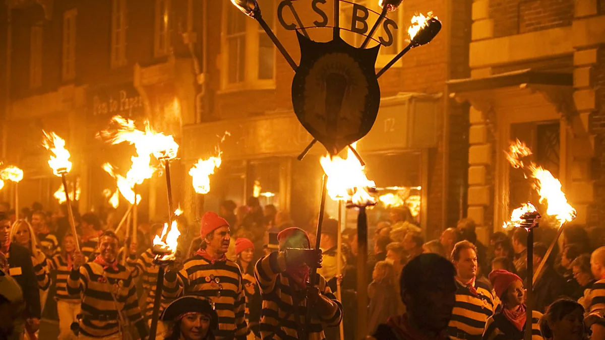 Commercial Square Bonfire Society members in yellow-and-black smugglers' jerseys carrying blazing torches and their society standard along a Lewes street