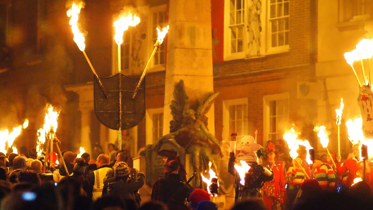 Torchbearers gathered around the War Memorial on Lewes High Street on Bonfire Night, a red Waterloo banner on the building behind